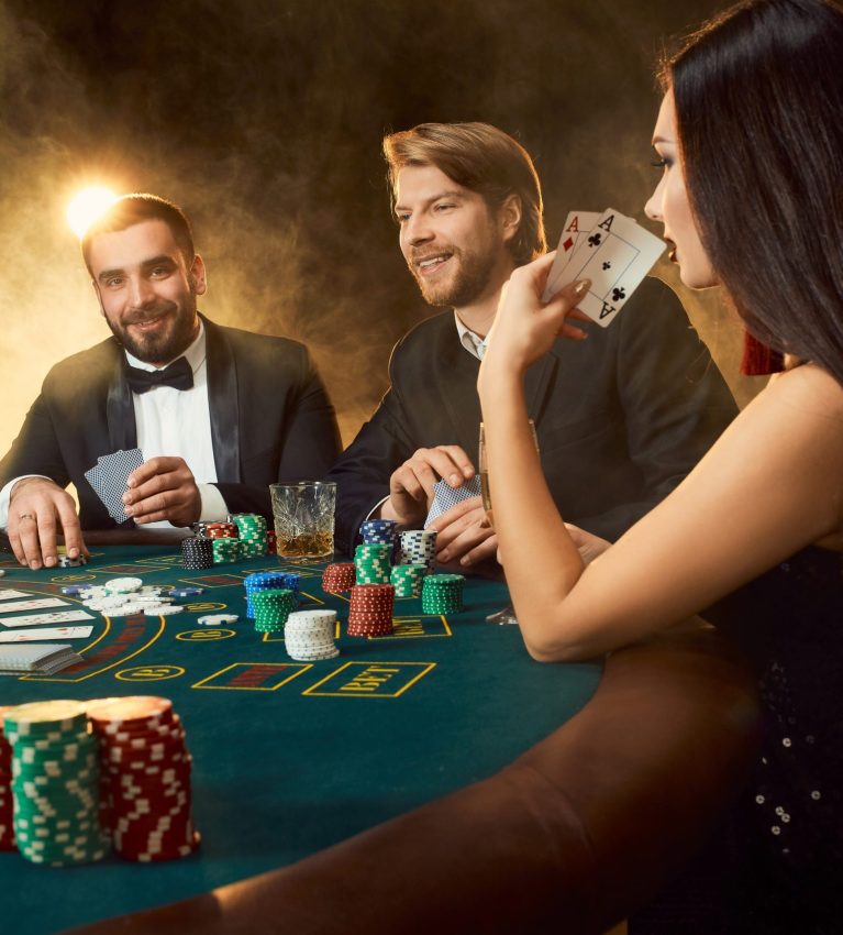 Group of young rich people is playing poker in the casino. Two men in business suits and a young woman in a black dress. Smoke. Casino. Poker